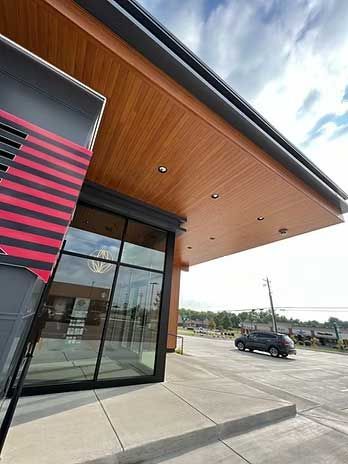 Exterior of a modern building with a wood-paneled overhang, large windows, and a black accent. A car is visible in the background.