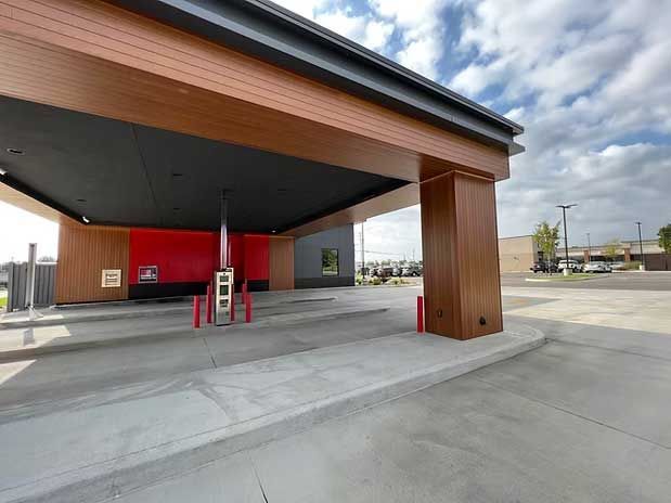 Drive-through bank area with concrete surface, brown wood accents, red walls, and a blue sky background.