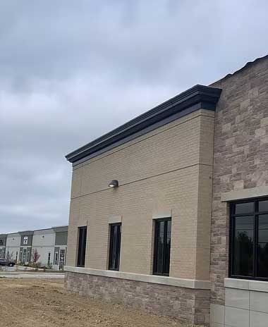 Exterior view of a commercial building with brick and stone, black trim, and windows under a cloudy sky.