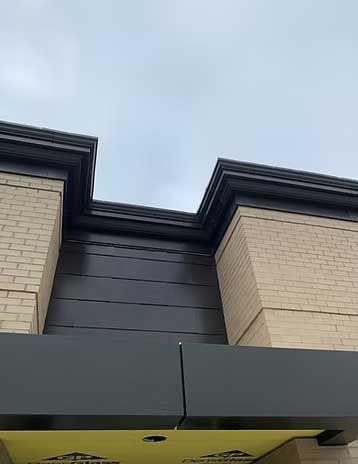 Exterior view of a building with light brick and dark gray trim under a cloudy sky.