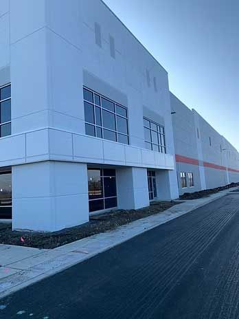 Large, modern industrial building with gray and orange accents. Blue sky background.