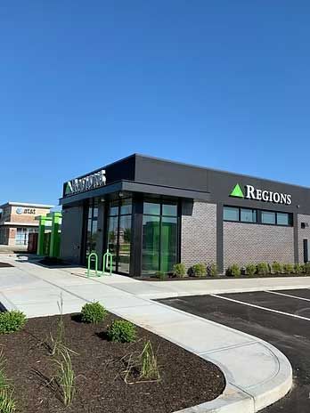 Regions bank building with gray brick exterior, glass windows, and green accents. Clear blue sky.