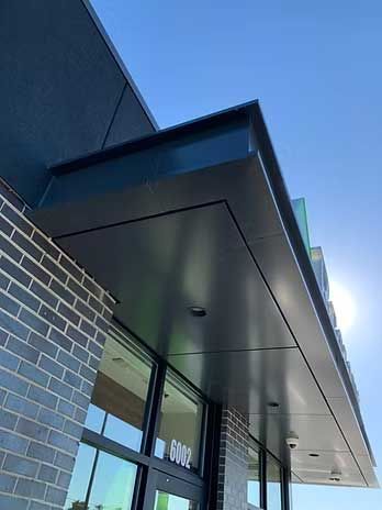 Exterior building with dark metal overhang and brick facade. Blue sky.