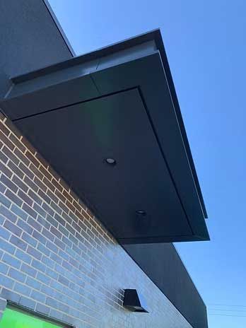 Dark gray awning extending from a brick building with two lights and a blue sky in the background.