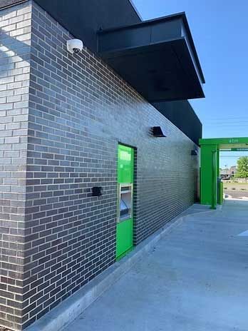 Exterior of a building with brick walls, a green door, and a drive-thru lane.