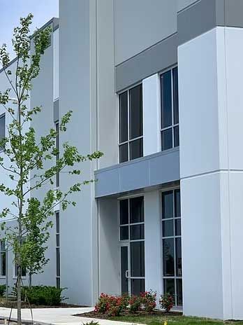 Modern, white building with large windows and a small tree in front.
