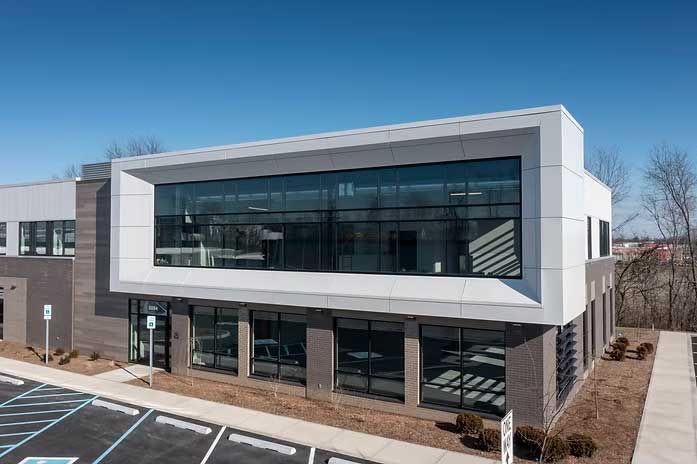 Modern commercial building with large windows and a gray and white facade against a blue sky.