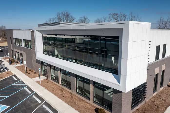 Modern office building with large windows and white and gray facade, clear sky.