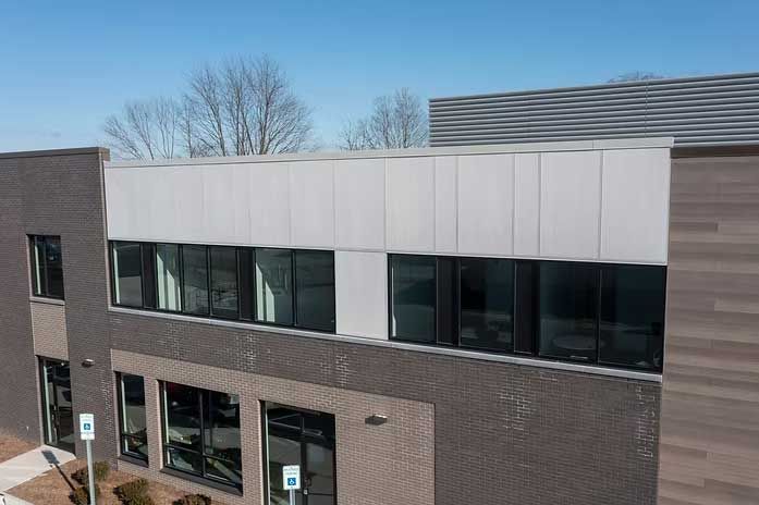 Modern brick building with a gray metal facade and large windows. Blue sky.