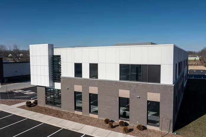 Modern two-story building with a white upper level and a gray brick lower level. Black windows and a clear blue sky.