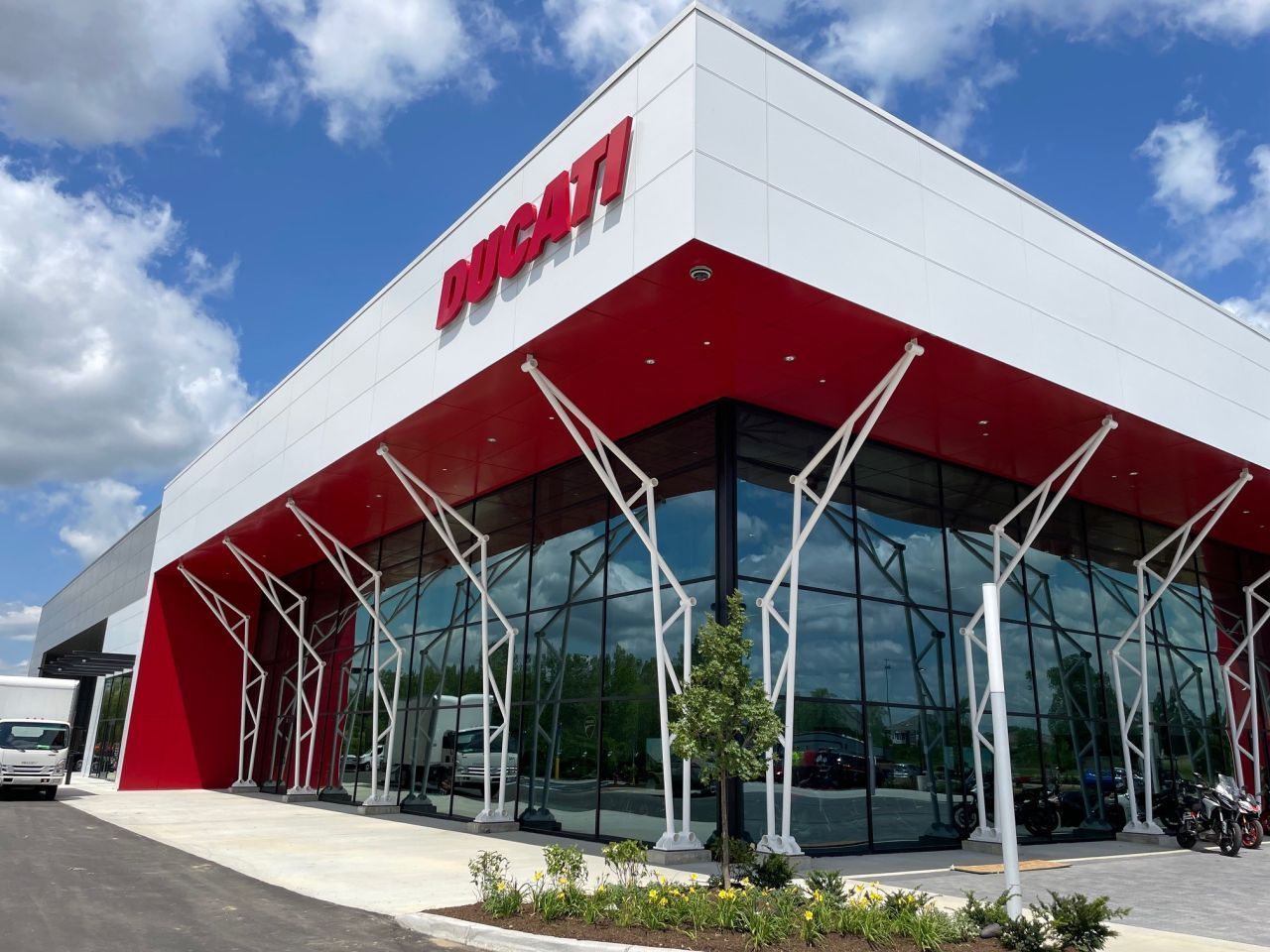 Ducati dealership exterior with red and white accents, large windows, and a blue sky background.