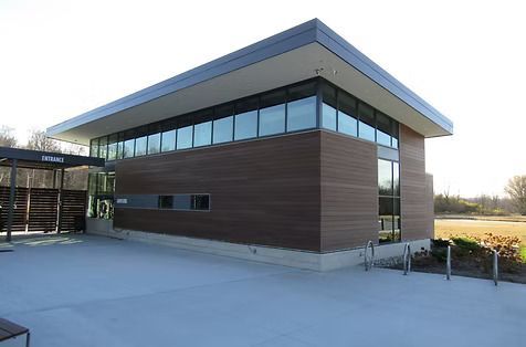 Modern building with brown wood siding and large windows, concrete patio, bike racks.
