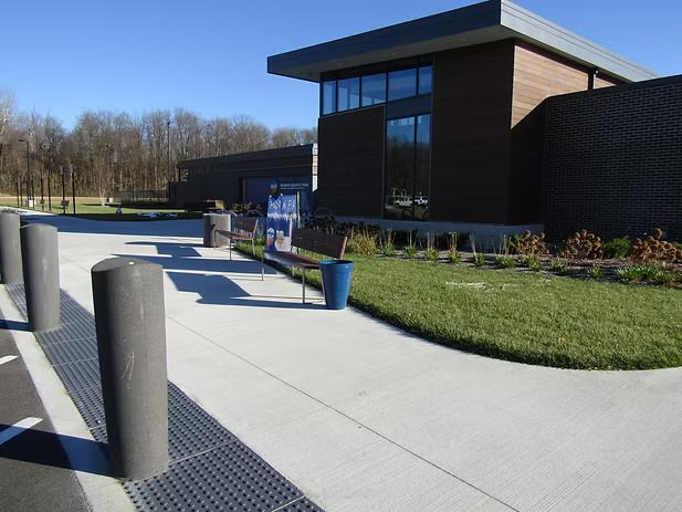 Exterior of modern building with concrete walkway, bollards, and landscaping.