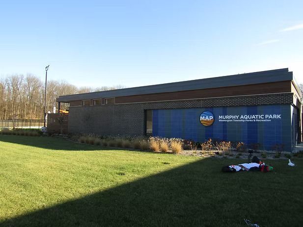 Exterior view of Murphy Aquatic Park building with blue sign, green lawn, and trees.