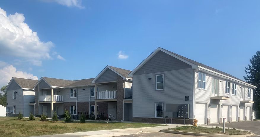 Multi-unit residential building with gray siding, balconies, and garage doors under a blue sky.