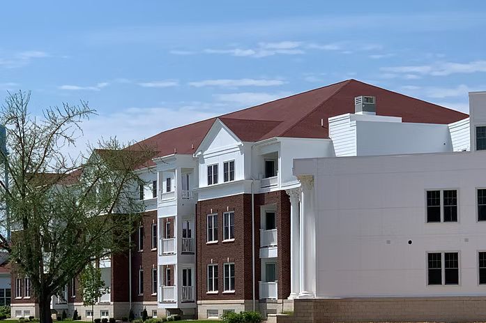 Multi-story brick and white building with a red roof under a blue sky.