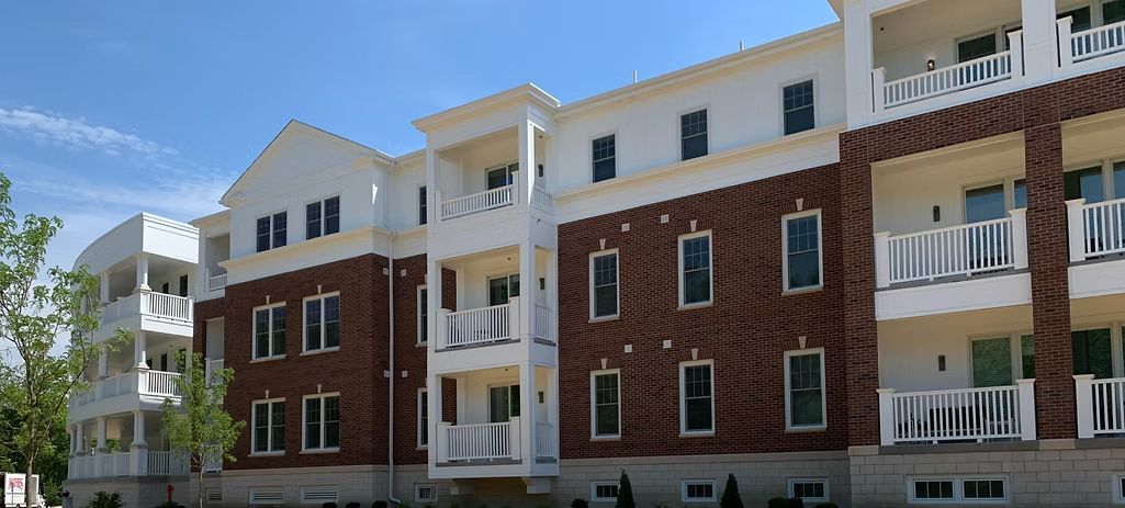 Multi-story brick and white apartment building with balconies, under a blue sky.