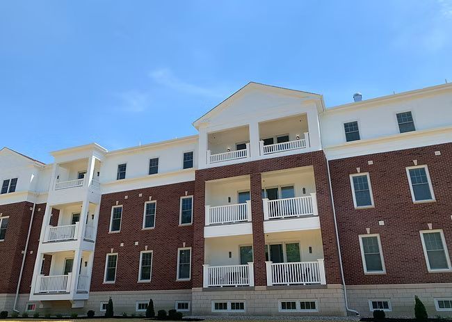 Multi-story brick building with white trim, balconies, and a blue sky.