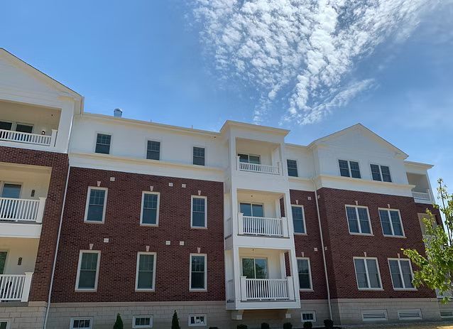 Multi-story brick and white apartment building with balconies, under a partly cloudy sky.