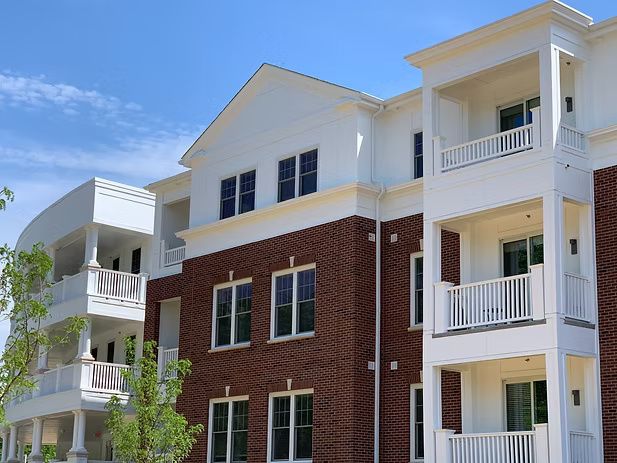 Multi-story brick and white apartment building with balconies and blue sky.