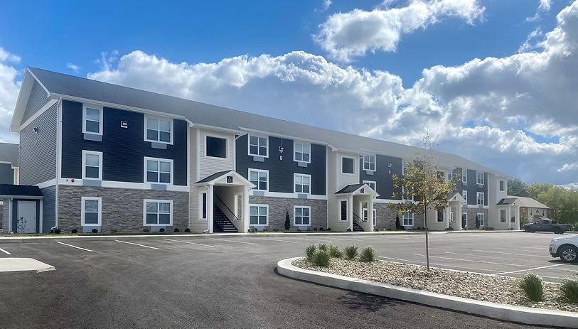 Multi-story building with blue siding, stone facade, and gray roof under a cloudy sky.