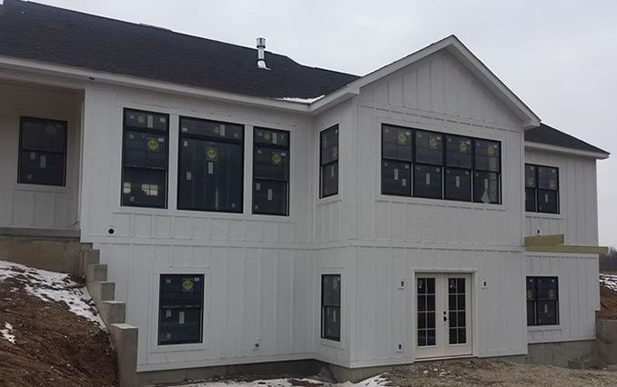White house exterior with dark-framed windows, vertical siding, and a black roof, in a winter setting.