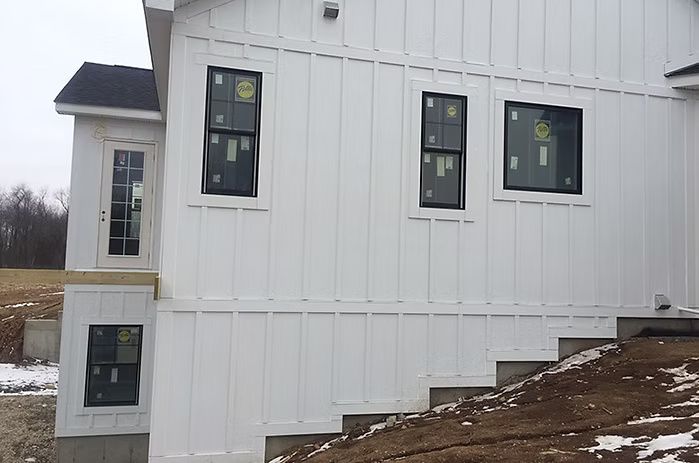 White house exterior with dark windows, door, and steps, under construction.