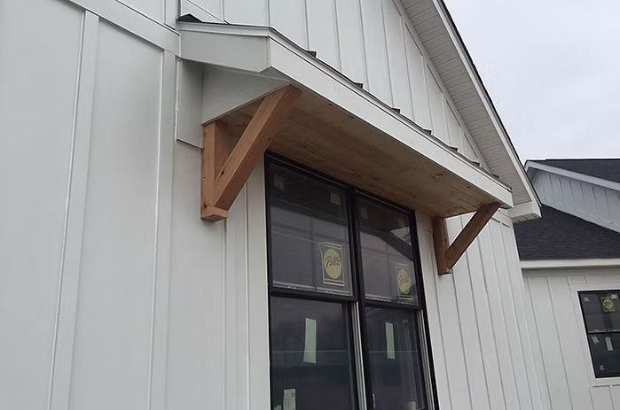 A light brown wooden awning above a dark-framed window on a white house.