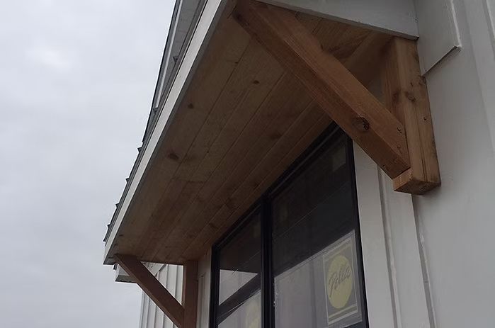 Wooden awning over a window on a white building, supported by angled brackets.