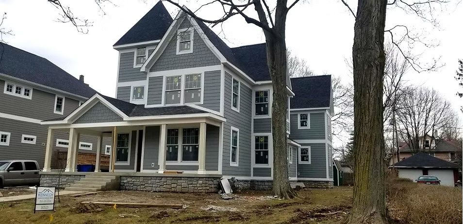 Gray two-story house with a black turret, covered front porch, and construction materials in the yard.