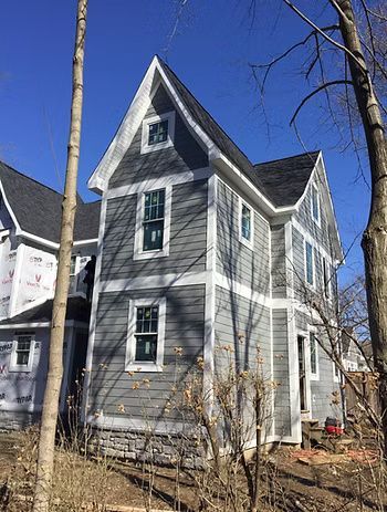Gray house with white trim against a blue sky, under construction.