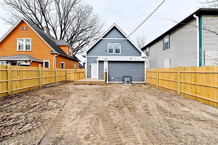 Backyard with a light blue building, wooden fence, orange house, and dirt.