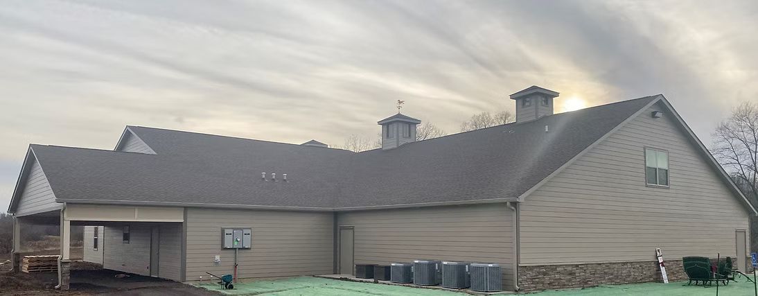 A tan building with a gray roof and air conditioning units out front under an overcast sky.