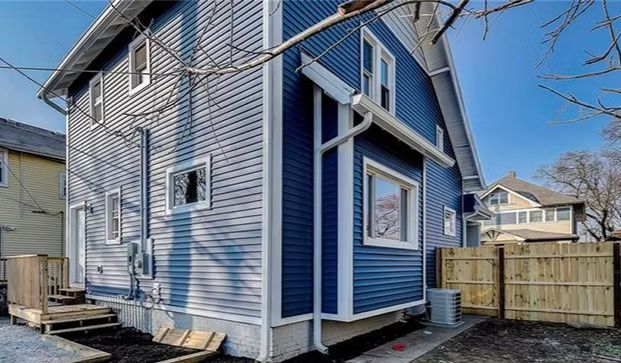 Exterior view of a two-story house with blue and gray siding, white trim, and a small wooden fence.