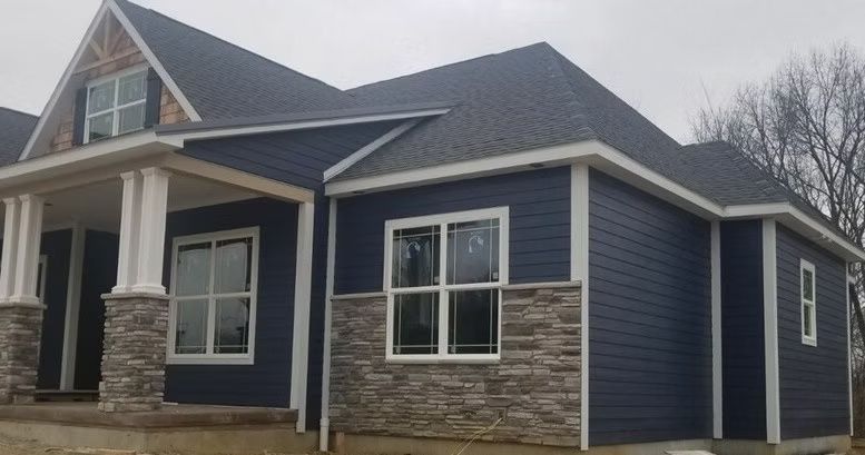 Blue house with stone accents and white trim under a gray sky.