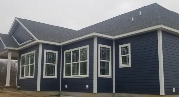Dark blue house with white trim and windows, under a gray sky.