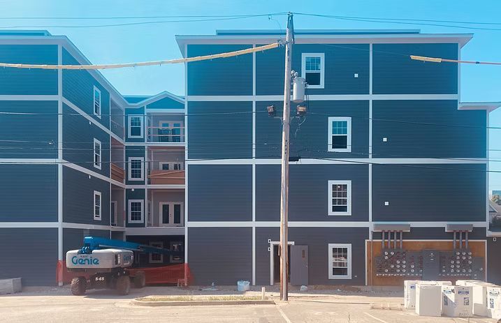 Multi-story apartment building under construction, blue siding, white trim, with a Genie lift.