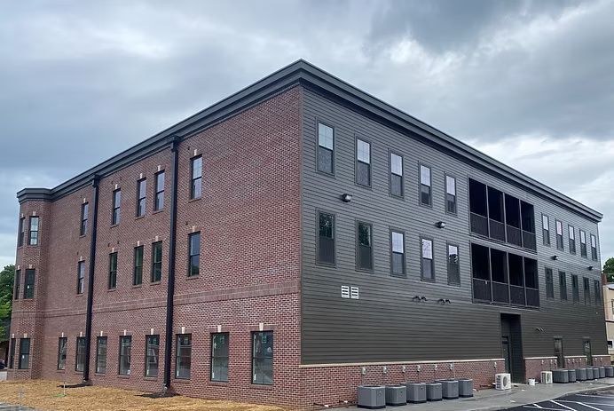 Three-story brick and black metal building with many windows, under a cloudy sky.