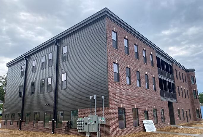Three-story building with brick and dark siding under a cloudy sky.