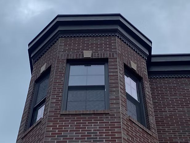 Brick building corner with three windows under a dark trim and a cloudy sky.