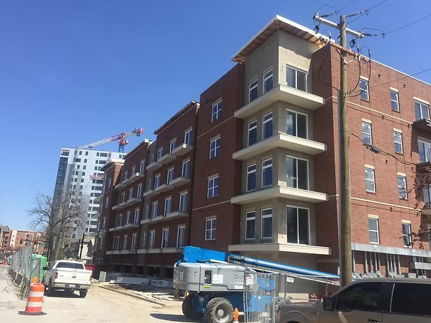 Multi-story brick building under construction with crane in the background, blue sky.