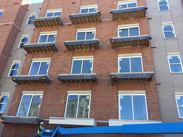 Brick building under construction with balcony platforms. A worker on a lift.
