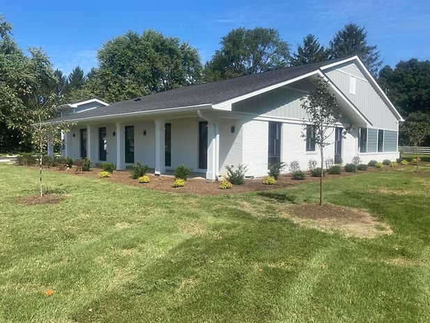 Light blue and white building with dark roof, small trees, and green grass.