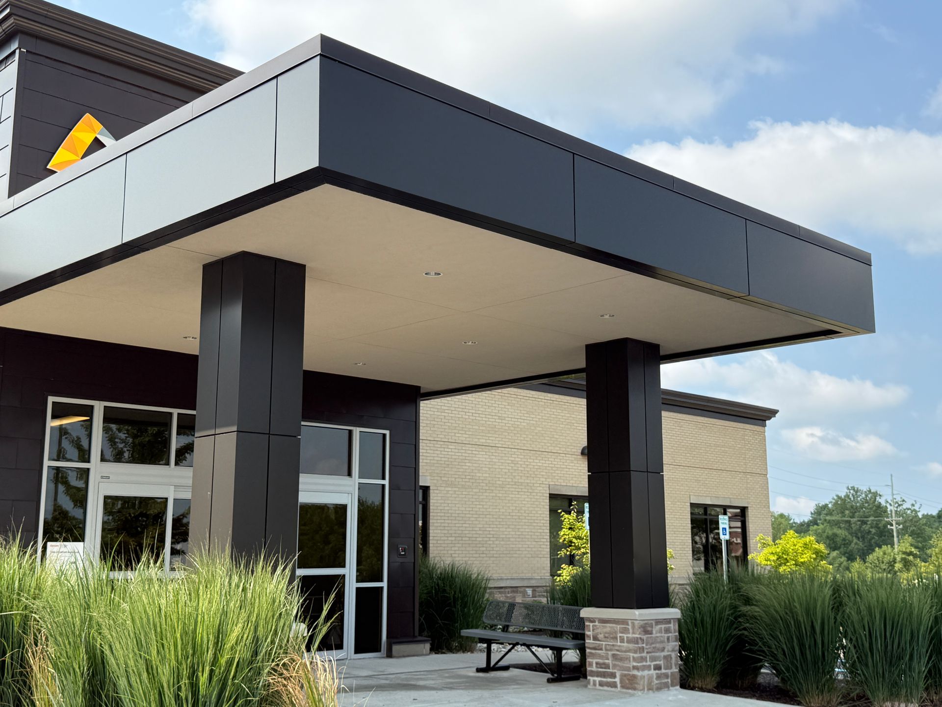Modern building entrance with a large dark canopy, glass doors, and landscaped grasses outside
