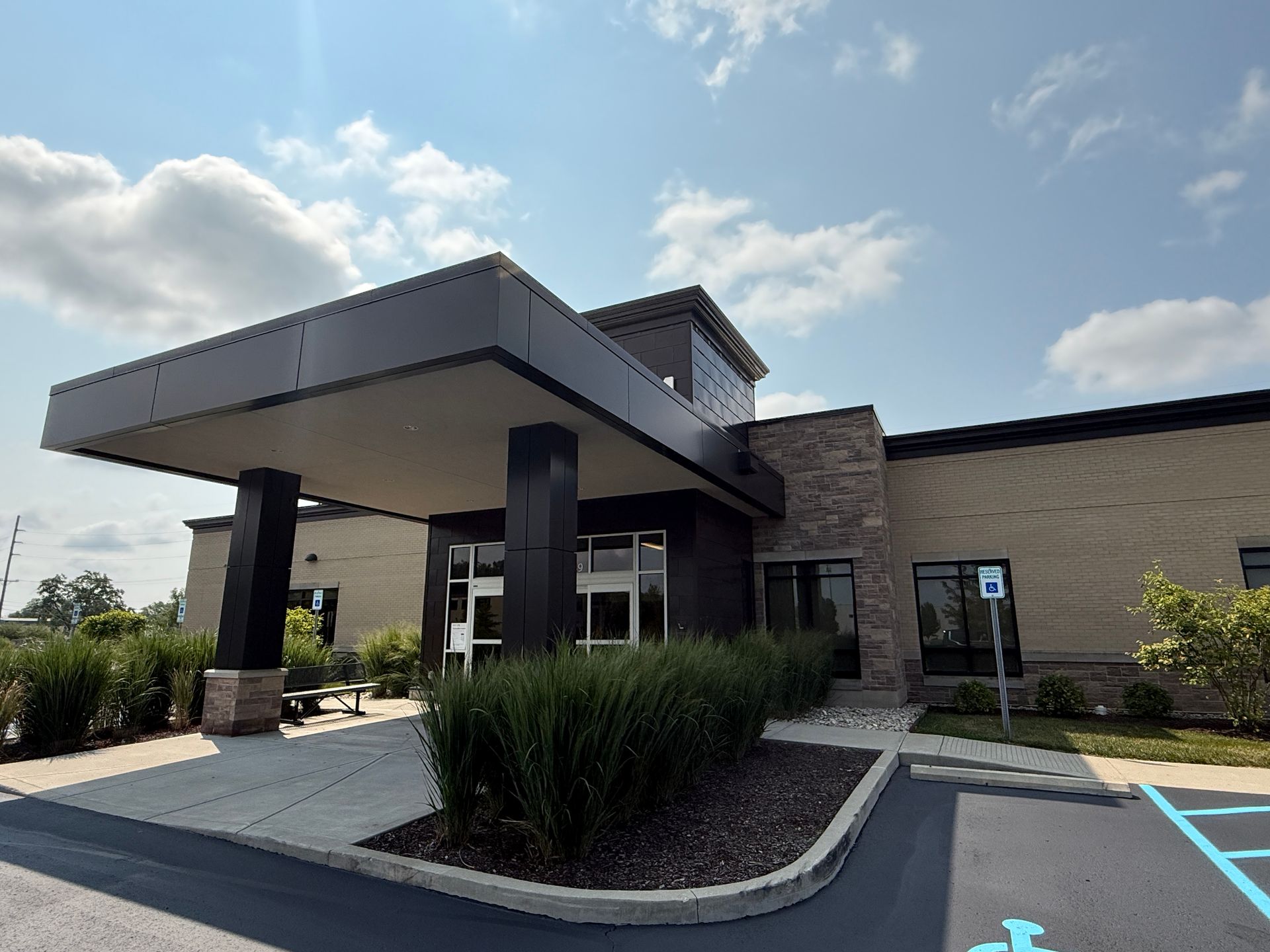 Modern building entrance with a covered drop-off canopy and landscaping under a blue sky