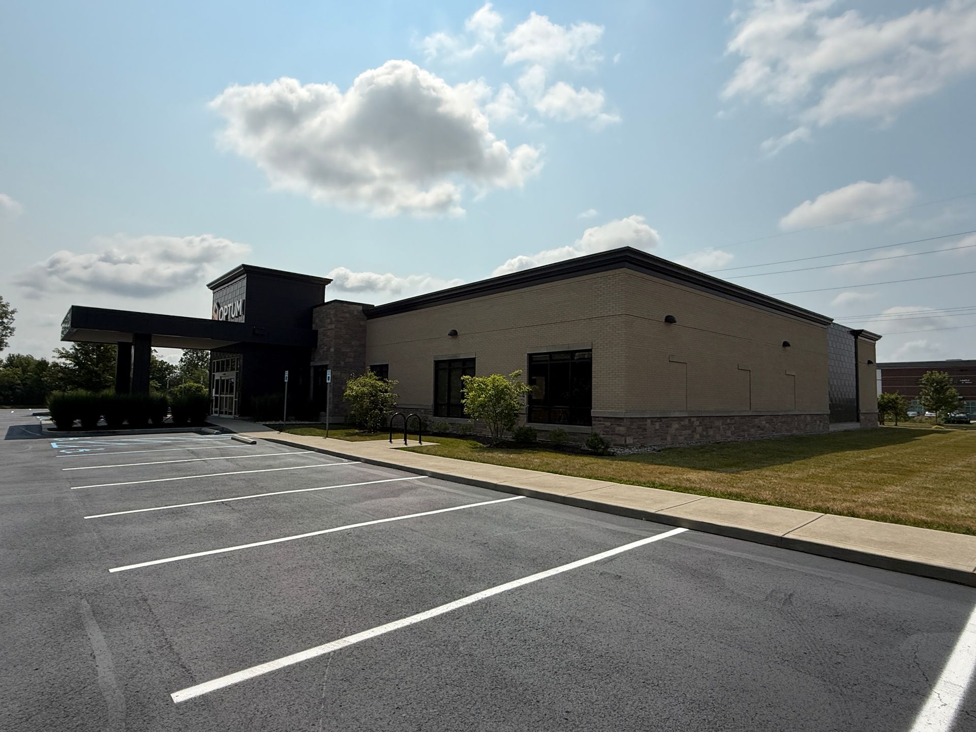 Brick building with black roof beside empty parking lot under a partly cloudy sky