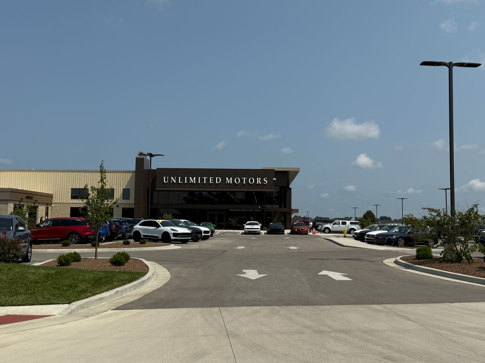 Wide view of a shopping center entrance with parked cars under a clear blue sky