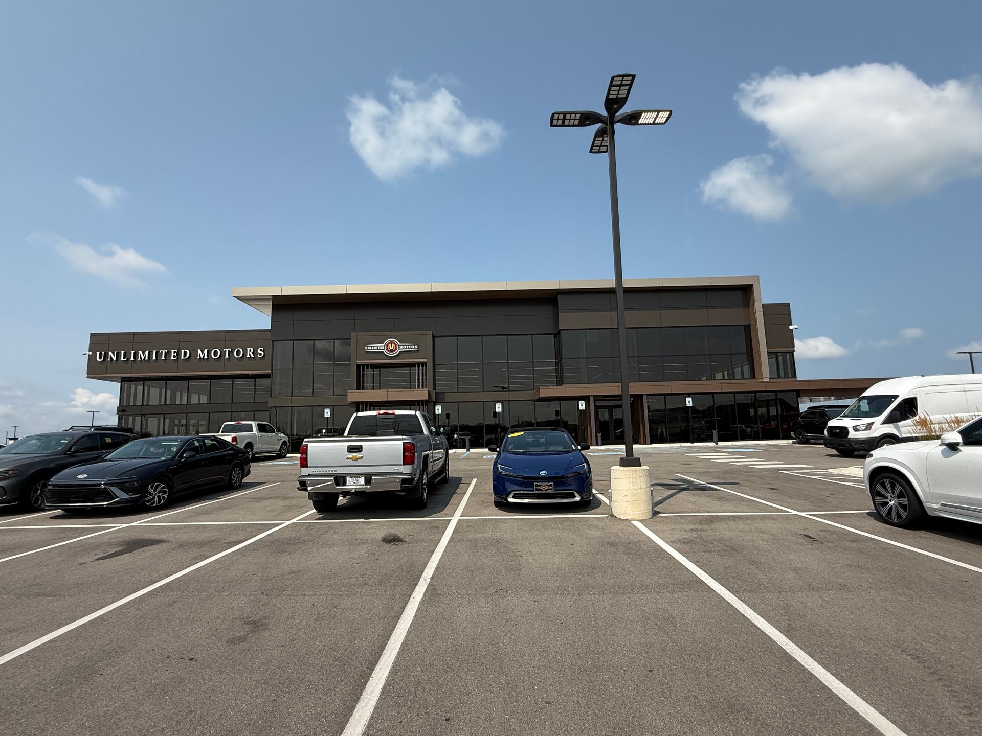 Parking lot in front of a modern hotel under a blue sky, with several cars parked outside.