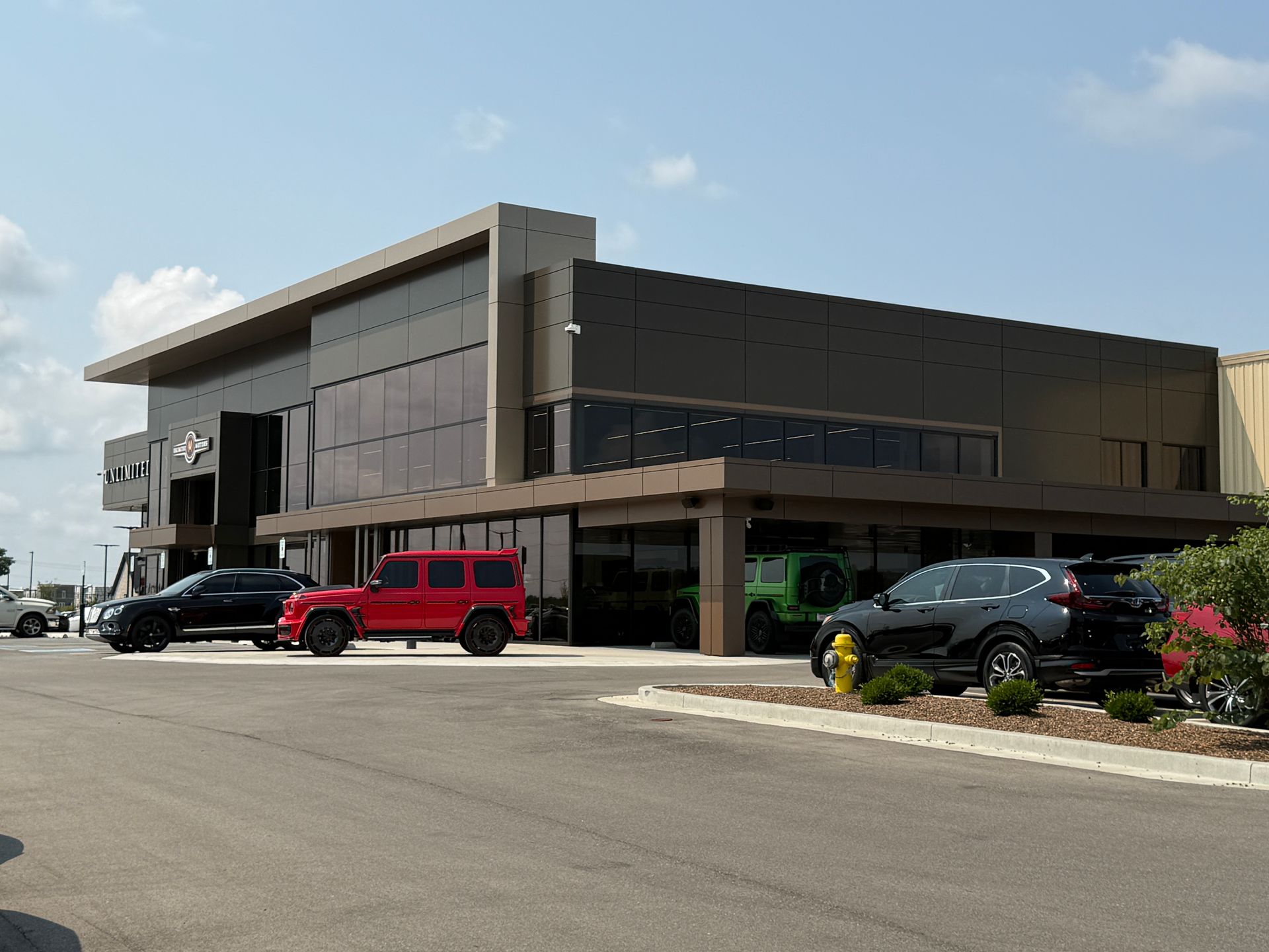 Modern office building with parked cars and a red SUV under a partly cloudy sky