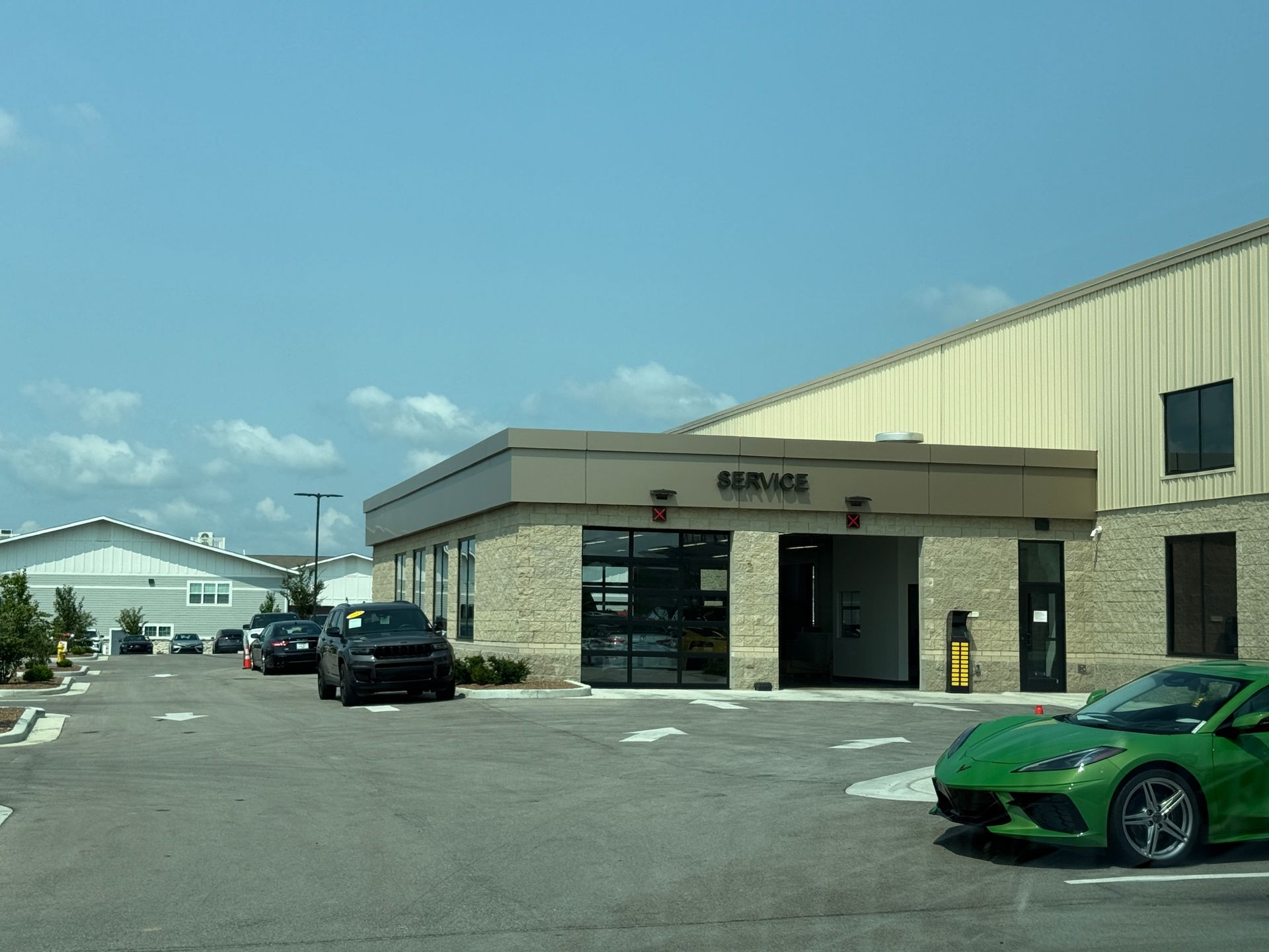 Small commercial building with parked cars, including a green sports car, under a clear blue sky